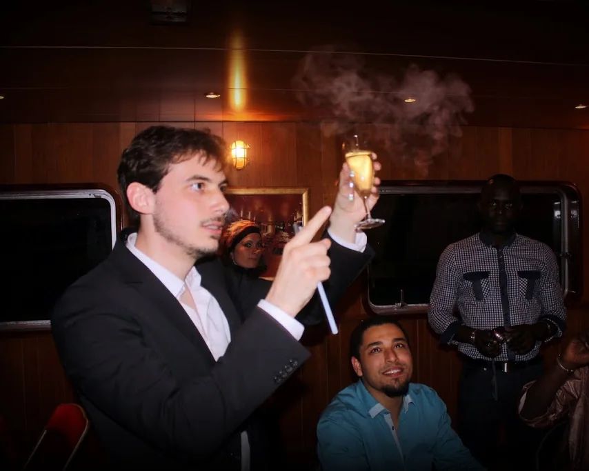 Vincent Wüthrich raises a glass trailing smoke, in front of guests