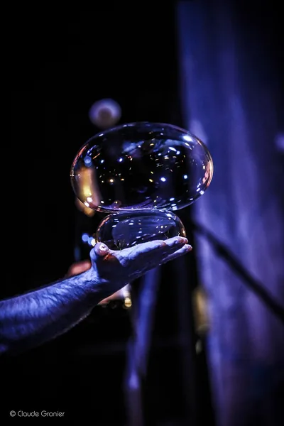 A large iridescent bubble resting on a hand, in blue light