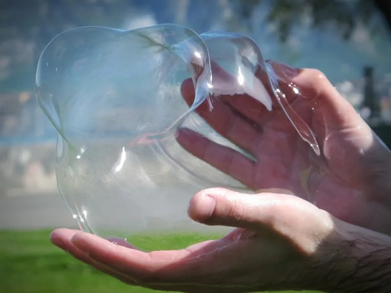 A large bubble resting between two hands, outdoors